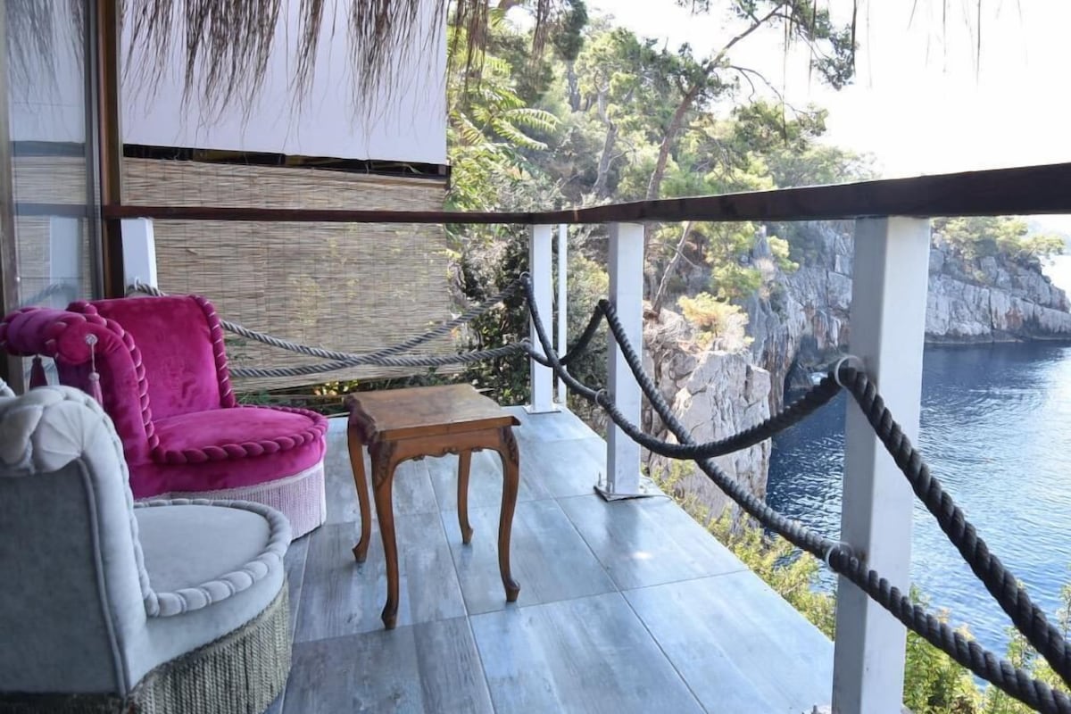 Un balcone con un divano in vimini, un piccolo tavolino e vista sul mare e sulle scogliere.