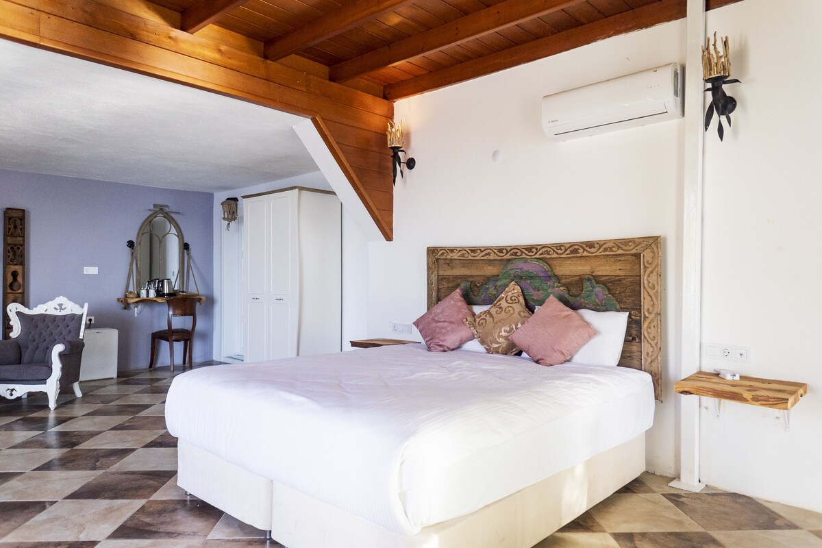 Una camera da letto con un letto grande, un soffitto in legno, una scrivania con una sedia e uno specchio appeso al muro.