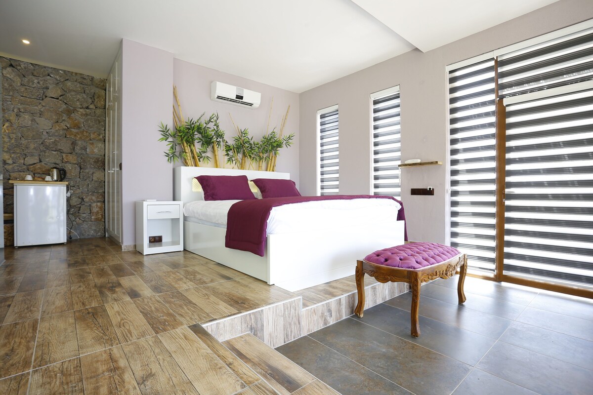 Camera da letto moderna con un letto, comodini, pavimento in legno, parete in pietra e ampie finestre con tende.