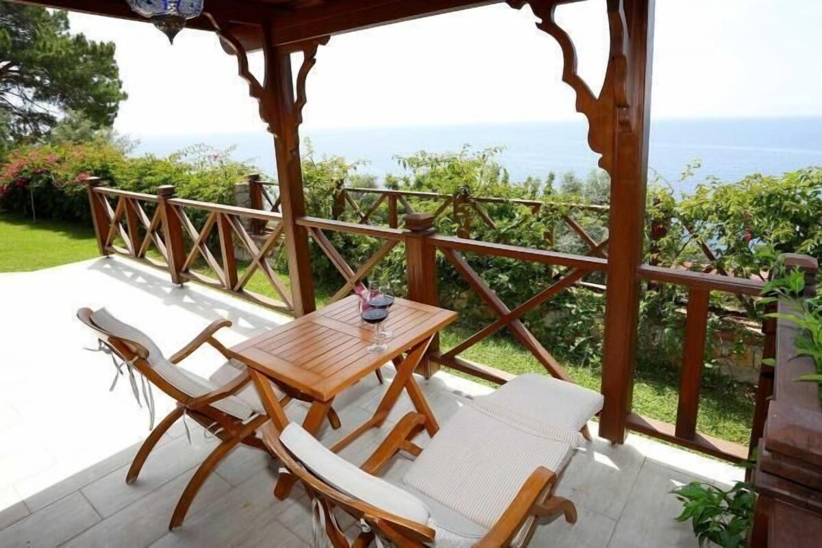 Un terrazzo in legno con tavolo e sedie, affacciato su un panorama mozzafiato del mare.