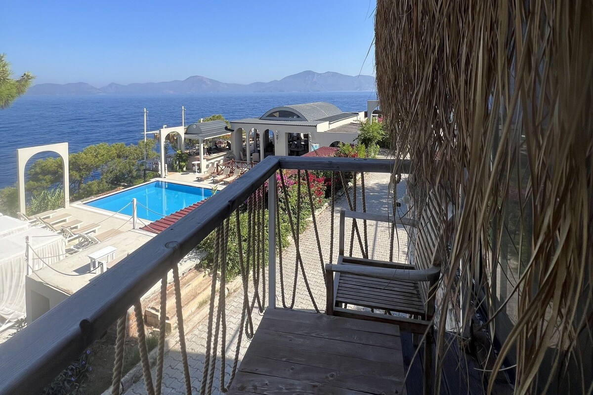 Una terrazza in legno con piscina, affacciata su un lago e montagne in lontananza.