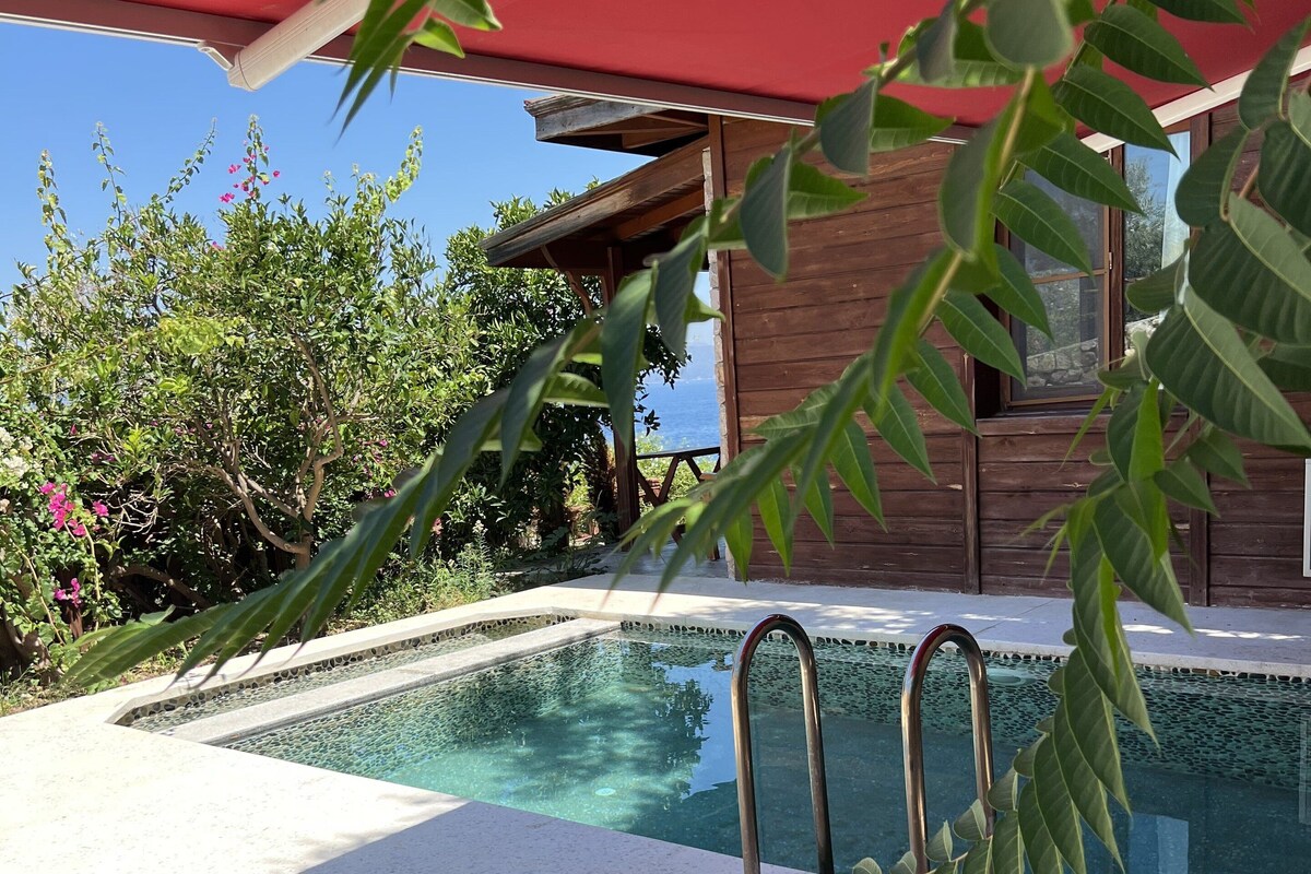 Zona piscina con una sedia a sdraio, un ombrellone rosso e un edificio in legno sullo sfondo.