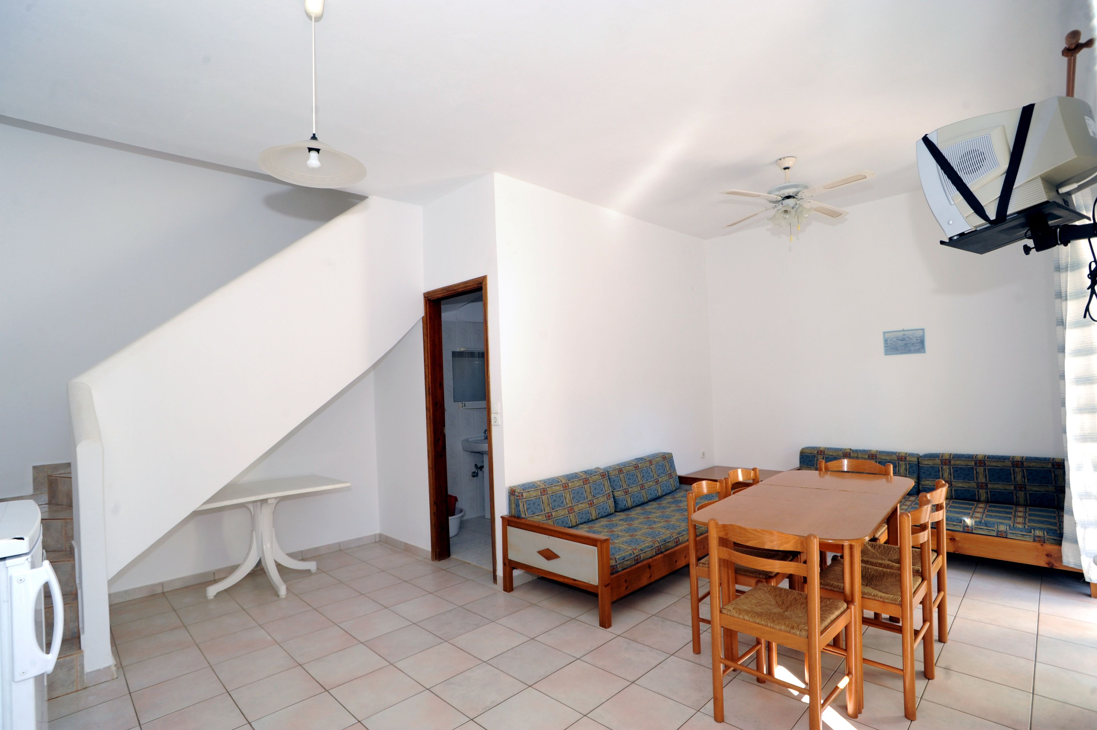 A room with a wooden dining table, a sofa, a ceiling fan, and a washing machine.