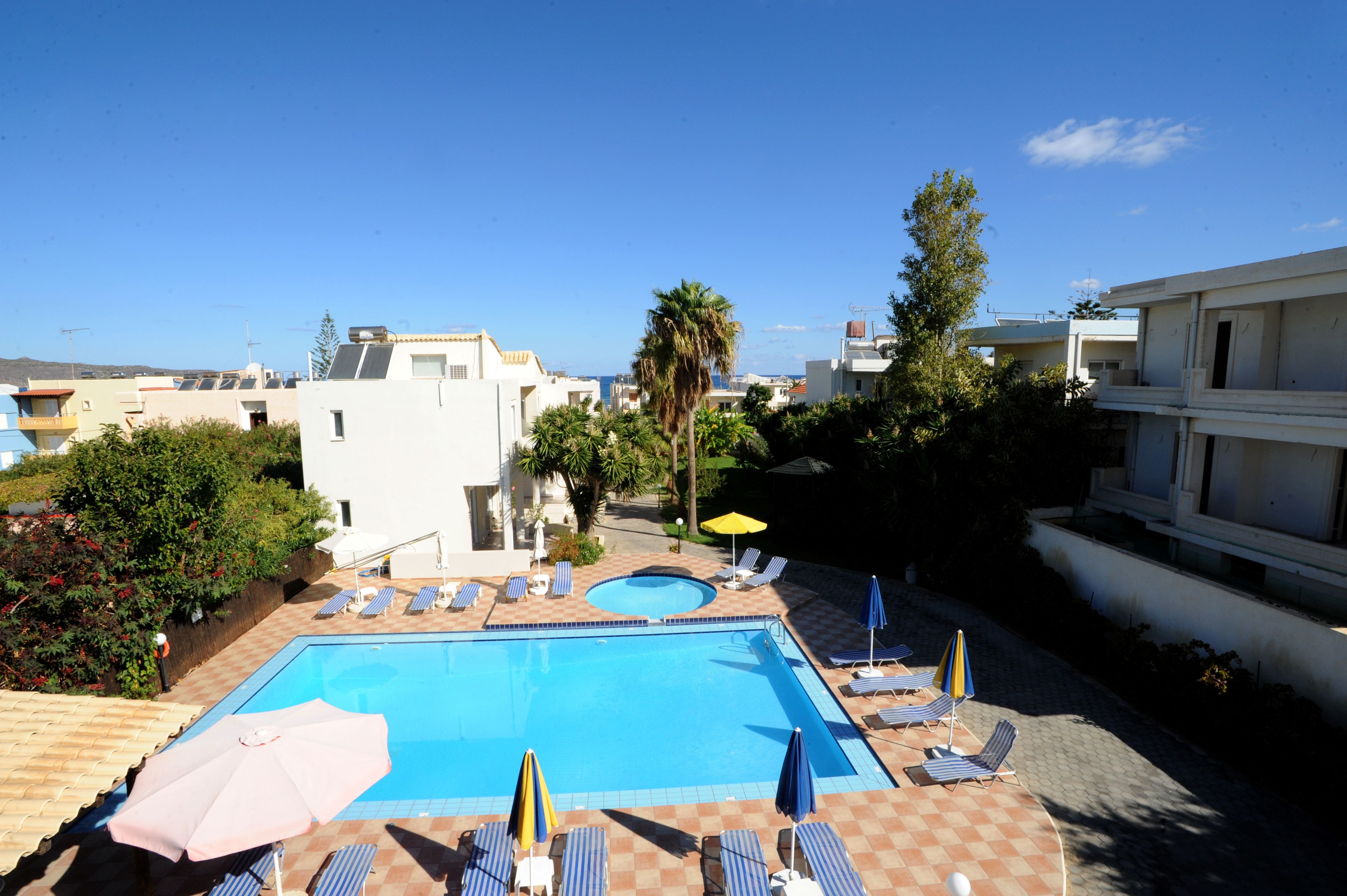 A swimming pool with lounge chairs and umbrellas, surrounded by greenery and buildings.