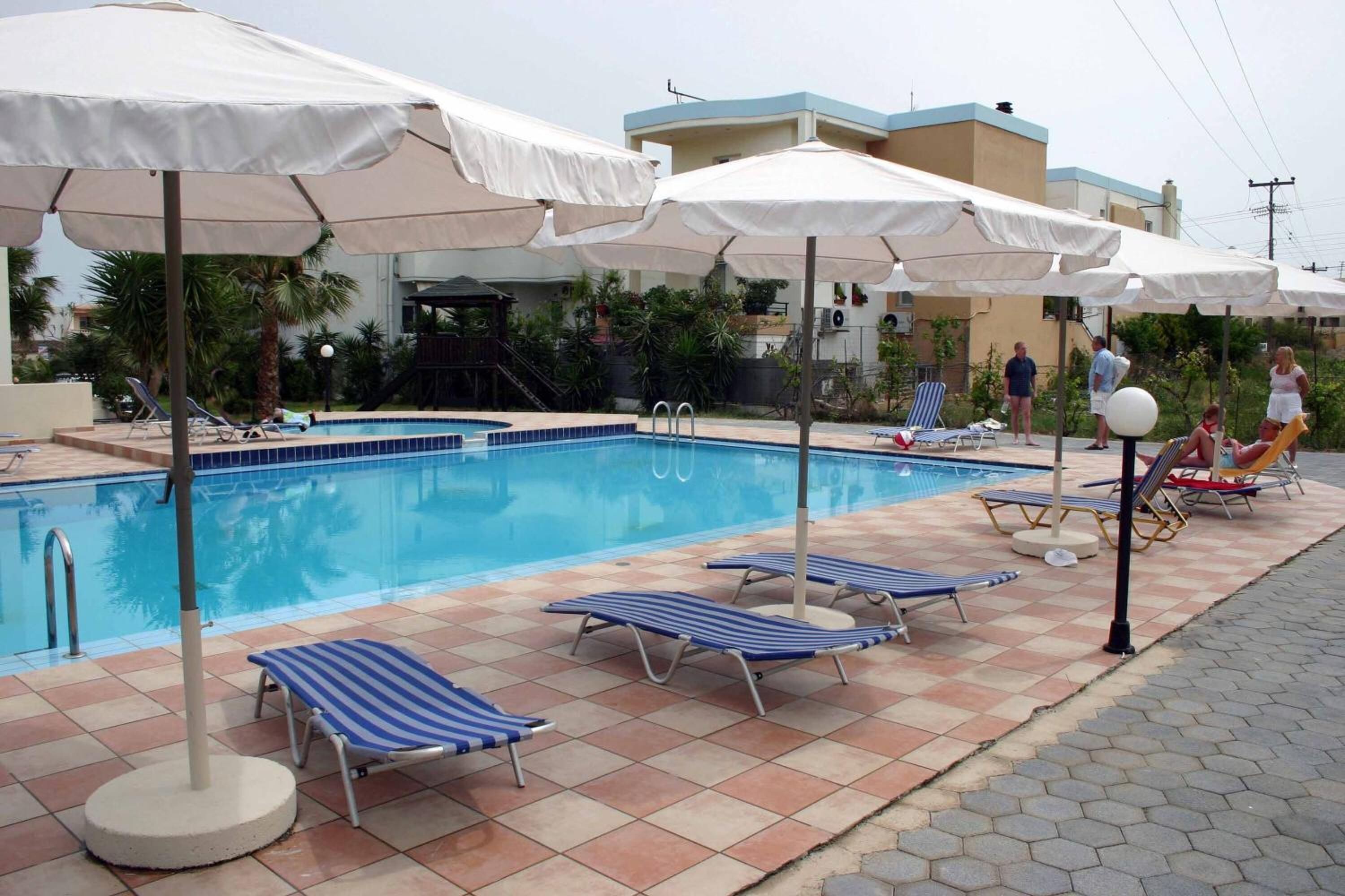 Una piscina con suelo de baldosas, sillones de descanso y sombrillas.