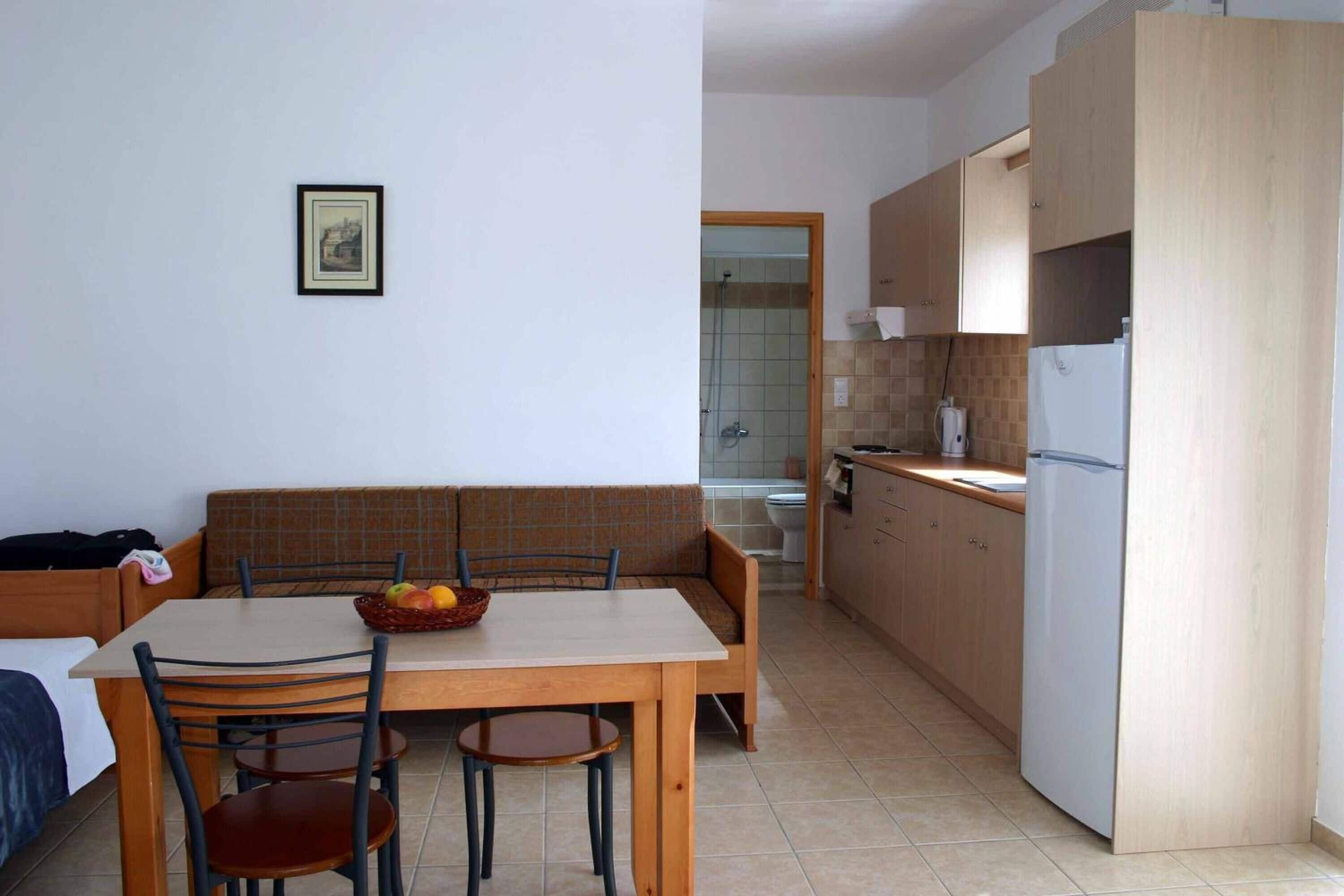 Une cuisine compacte comprenant une table à manger, des chaises et un banc intégré. On peut voir un réfrigérateur et un évier.