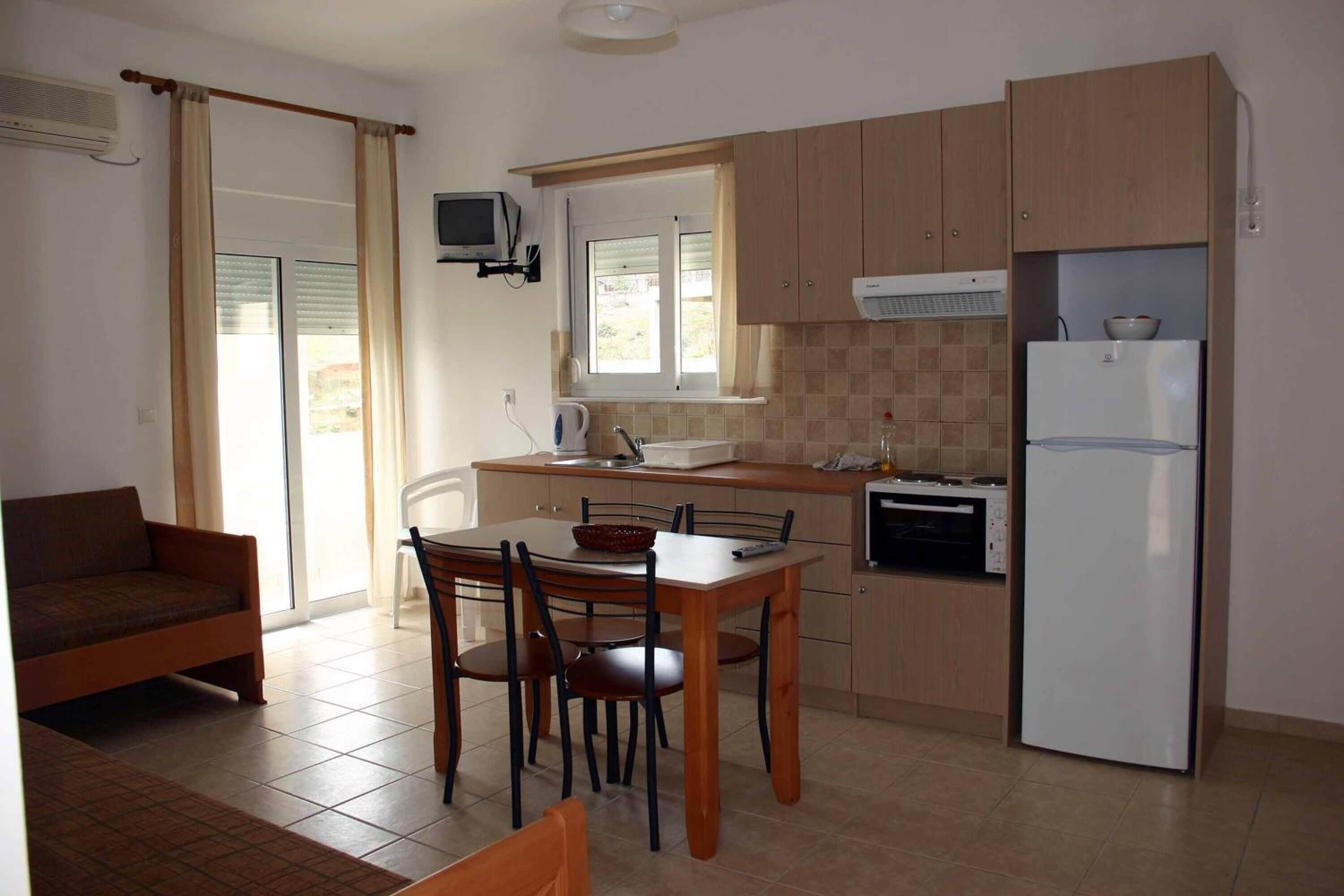 Una cocina compacta con comedor, un sofá y un televisor montado en la pared.