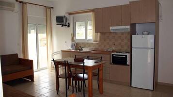 Una cocina compacta con comedor, un sofá y un televisor montado en la pared.