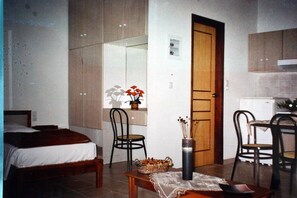 A bedroom with a bed, a chair, a small table with a vase, and a wooden door. - Evilion Hotel (Chania)