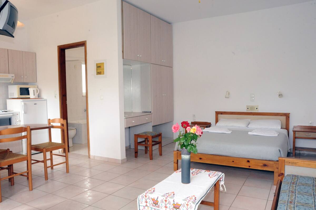 Un dormitorio con cama, mesita de noche y una pequeña mesa con un jarrón de flores.