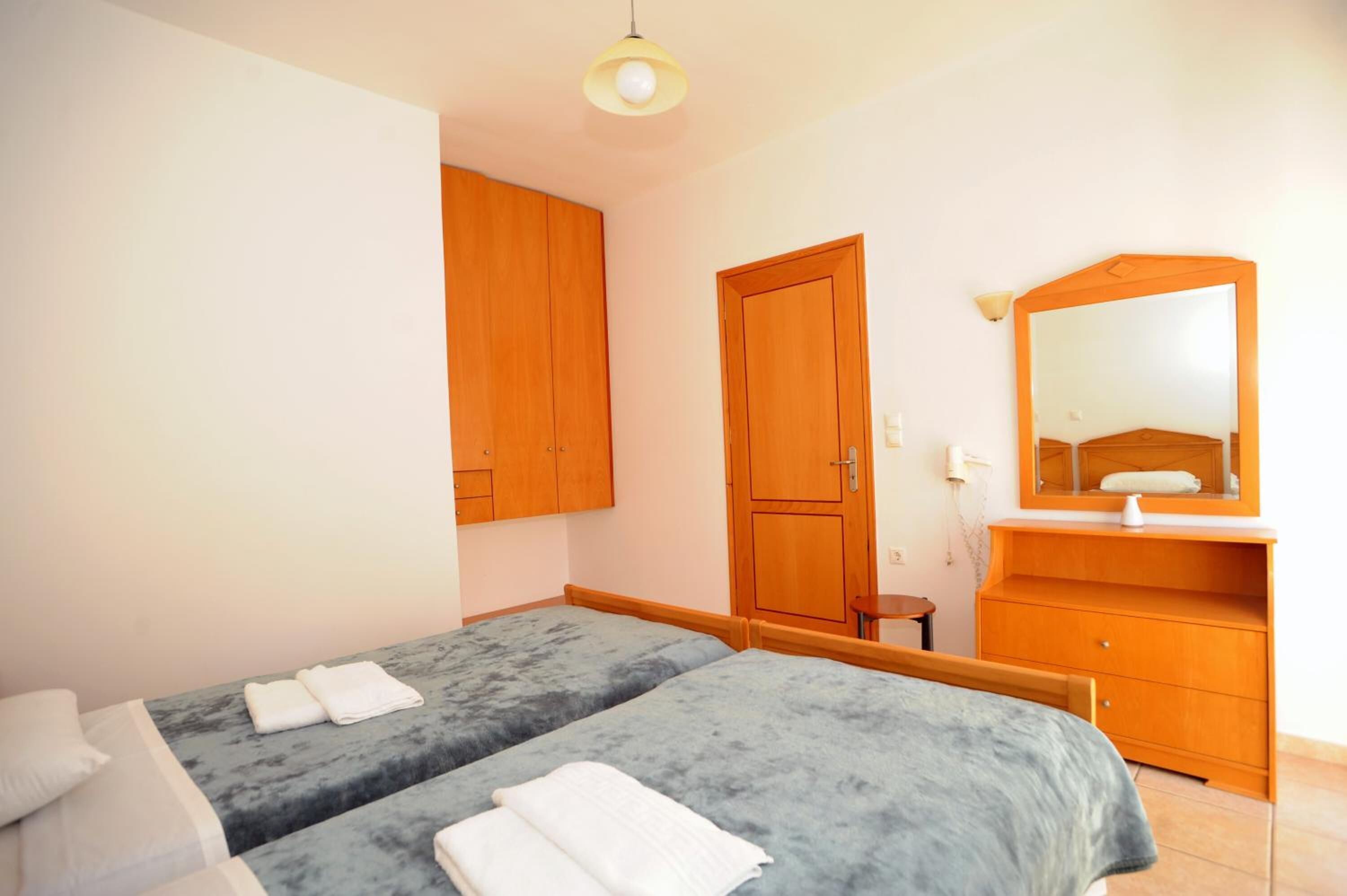 A bedroom with two beds, wooden wardrobe, and a mirror.