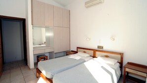 A bedroom with two single beds, a wooden wardrobe, a small table, and a mirror. - Evilion Hotel (Chania)