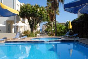 A swimming pool with blue tiles, surrounded by lounge chairs and umbrellas. - Evilion Hotel (Chania)