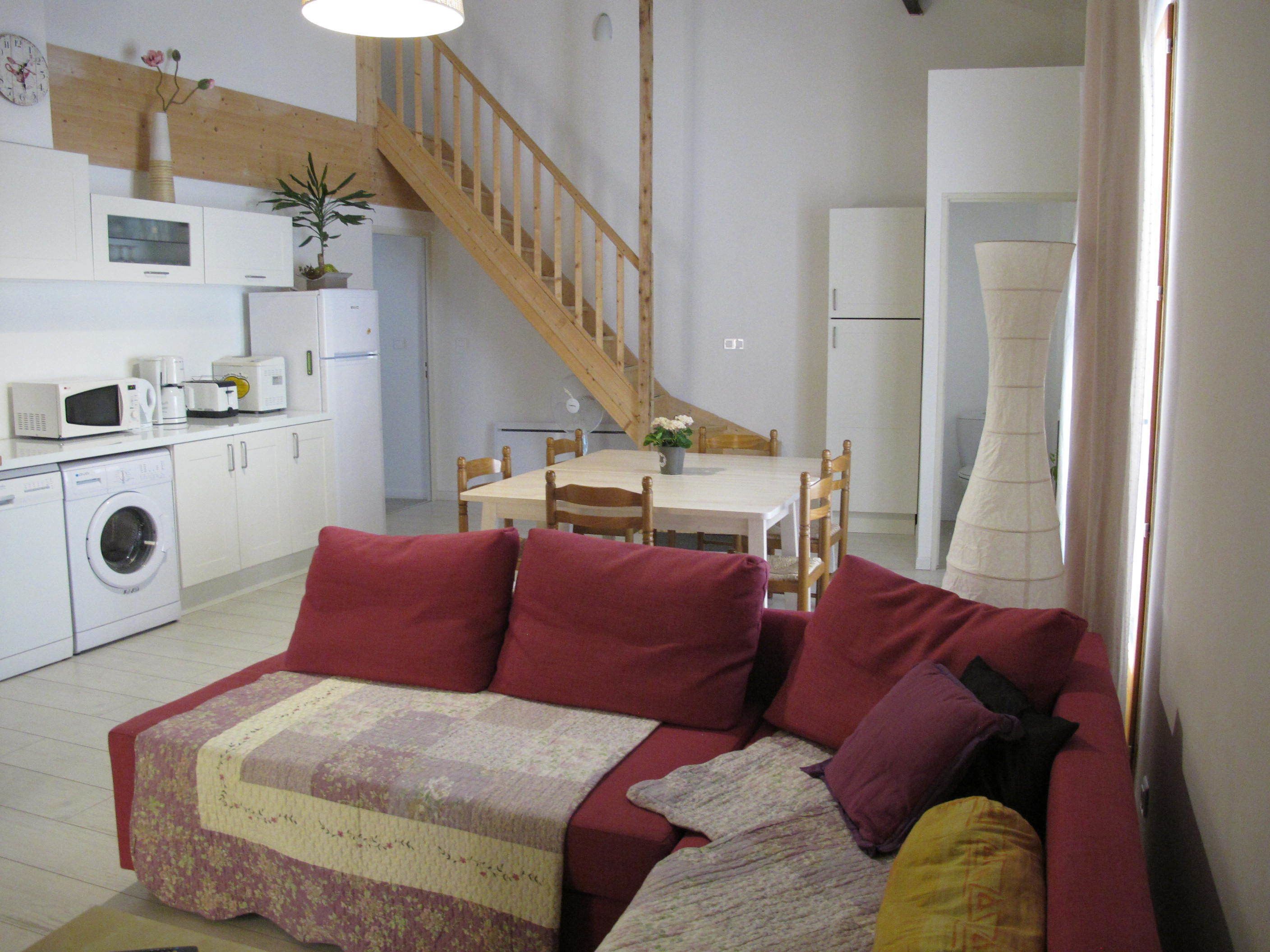 A living room with a red sofa, a wooden staircase, a dining table with chairs, a washing machine, and a microwave.