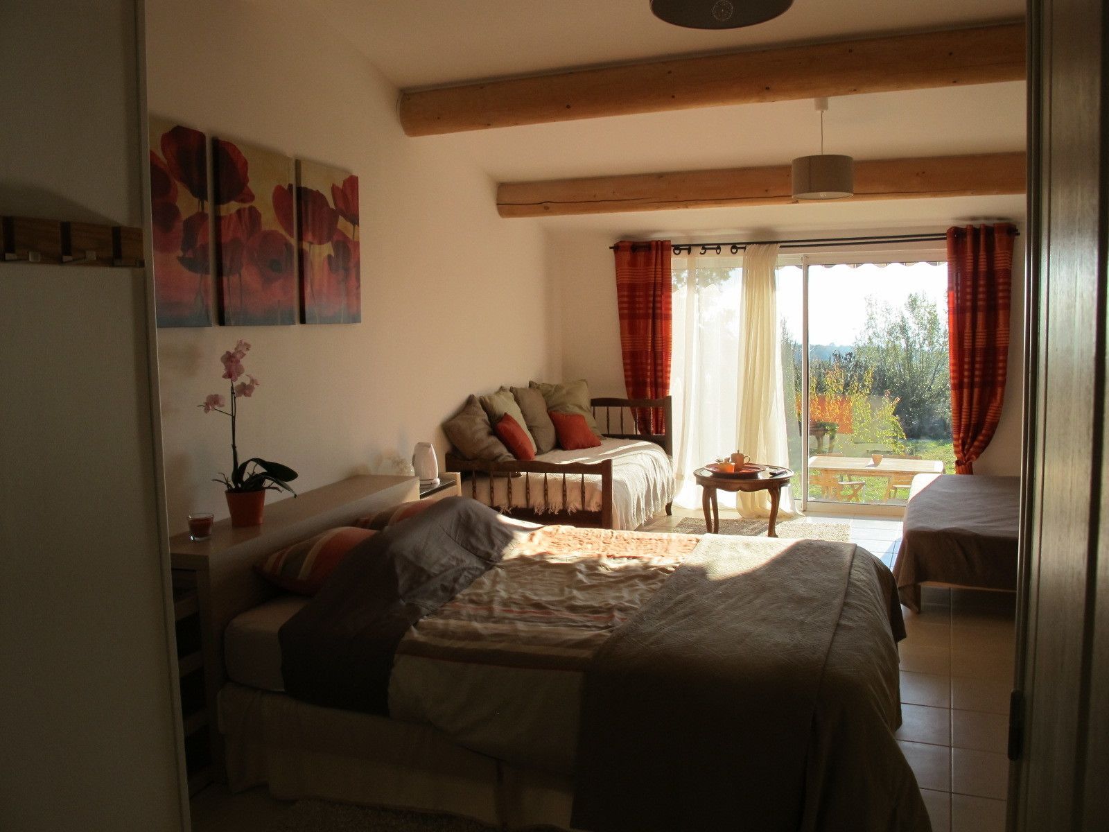 Een knus slaapkamer met een bed, een klein tafeltje en een stoel. Er is een balkon met uitzicht op bomen en een tafel buiten.