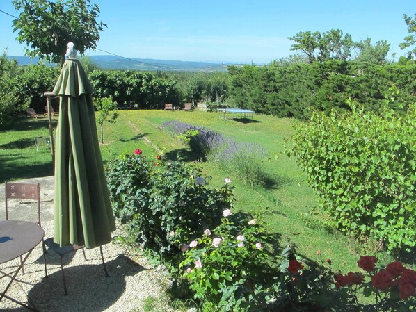 A garden with a table and chairs, a statue, and a view of the landscape.