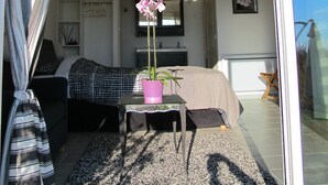 A modern interior with a bed, a small table with a pink vase, and a view of the outside. - Loucardalines (Bedoin)
