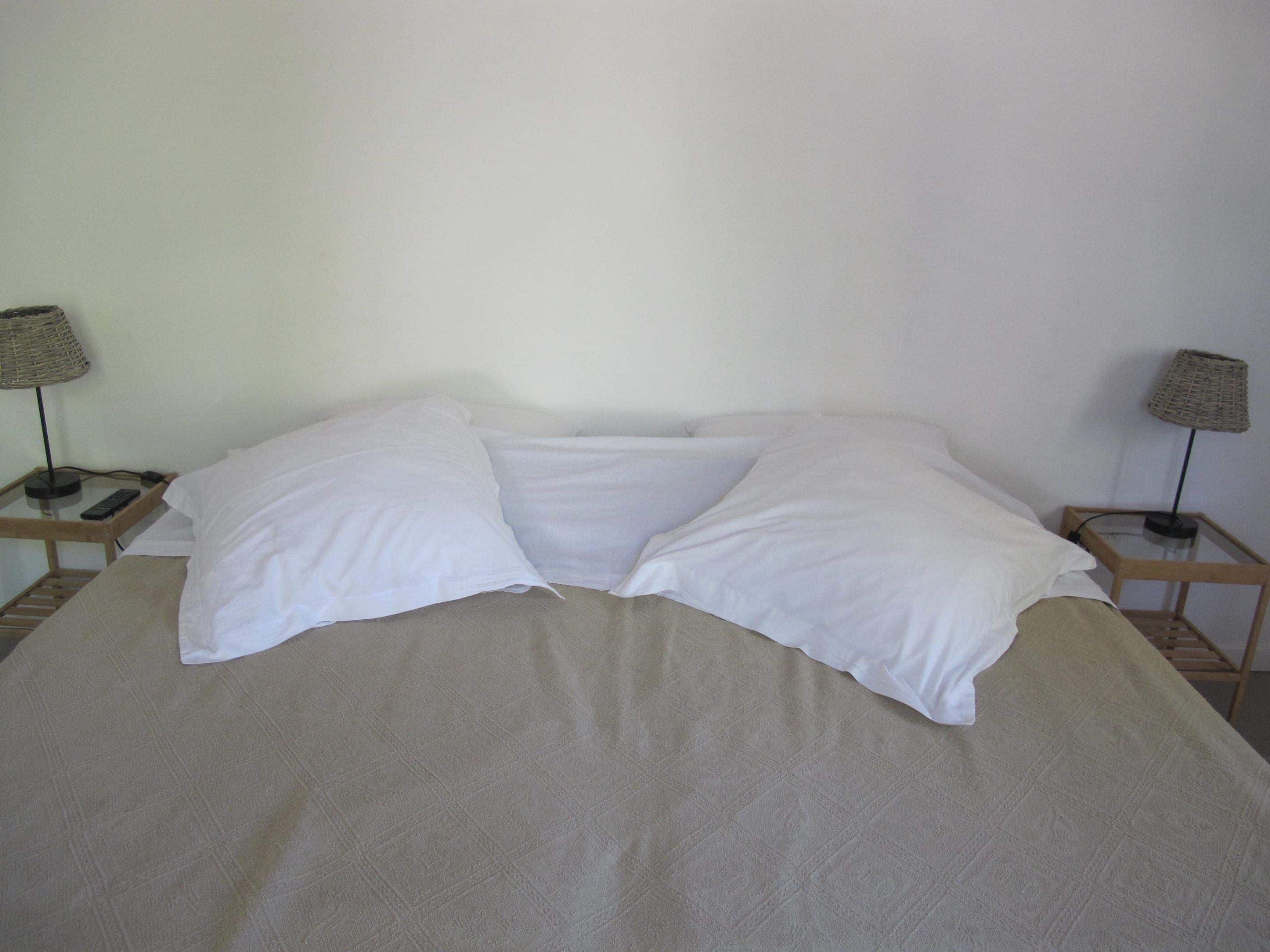 Een bed met witte lakens, twee nachtkastjes met lampen en een effen muur.