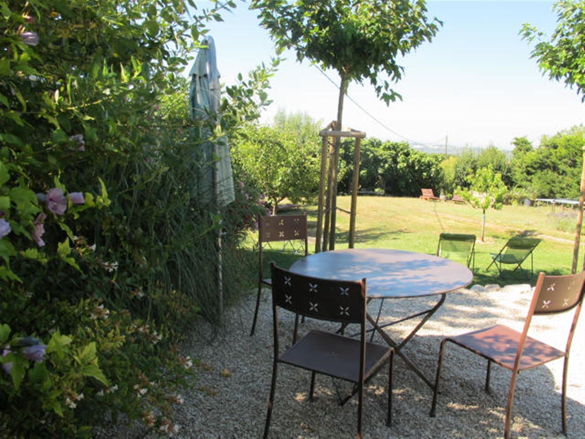 A patio with a round table and four chairs, surrounded by greenery and a clear sky.