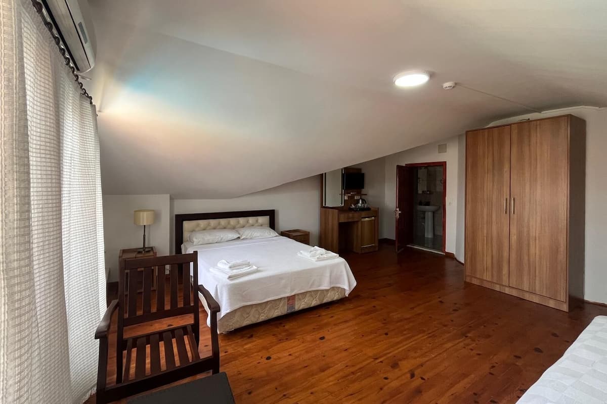 A bedroom with a bed, wooden wardrobe, and a desk with a chair.