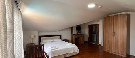 A bedroom with a bed, wooden wardrobe, and a desk with a chair.