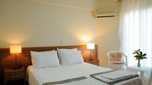 Habitación de hotel con una cama grande, dos lámparas de noche, una silla, una mesita con un florero y un equipo de aire acondicionado en la pared.