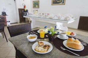 Una escena de desayuno con una mesa de vidrio, platos de comida, un florero y una taza de café.