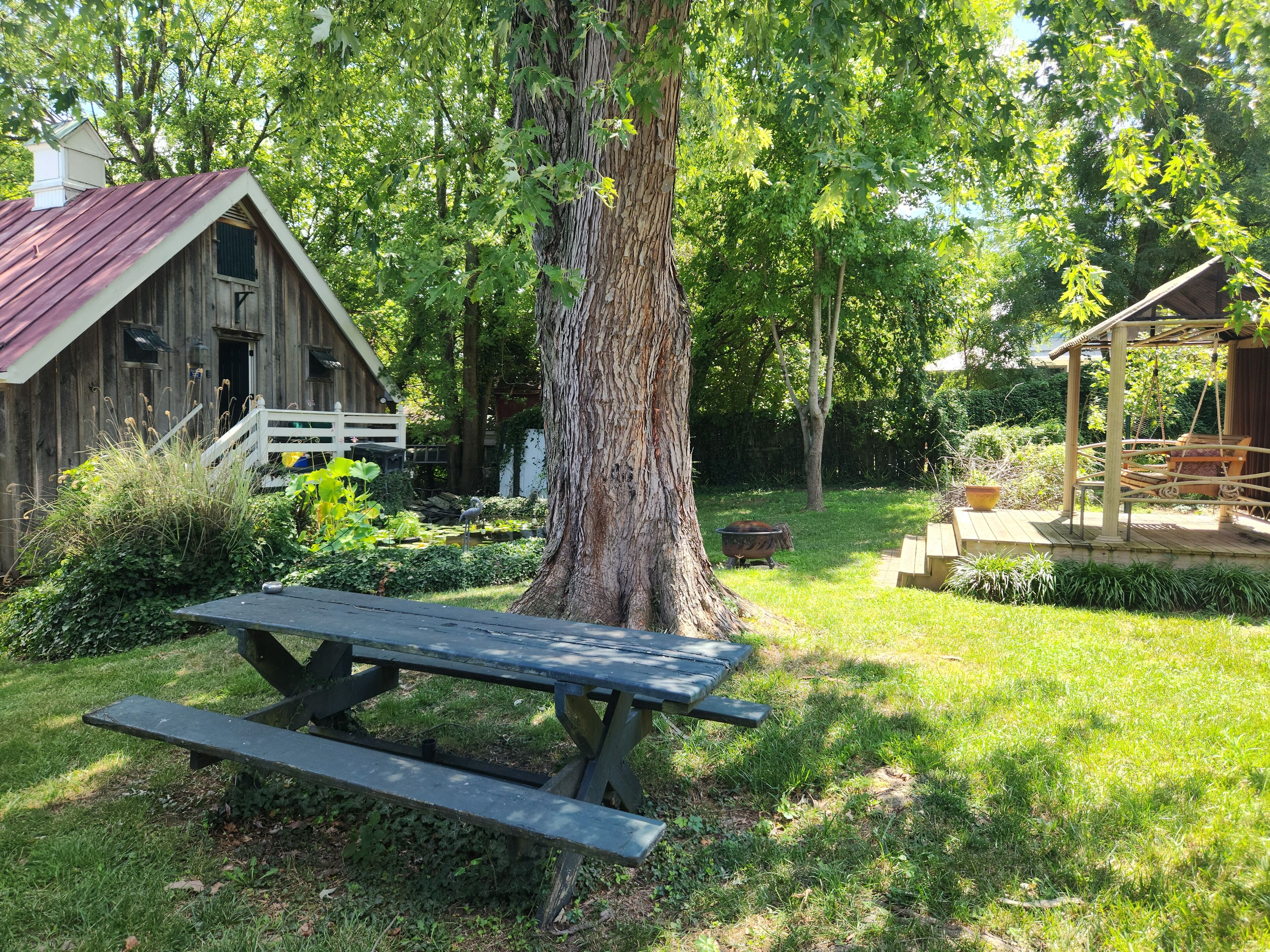 A rustic wooden cabin with a red roof, a picnic table, and a swing set in a lush garden.