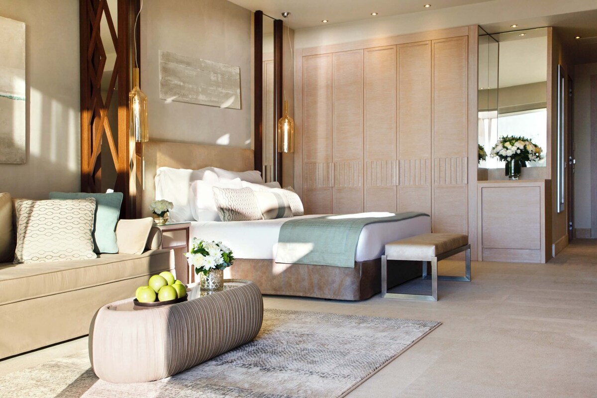 A modern bedroom with a large bed, a sofa, a bench, and a wardrobe.