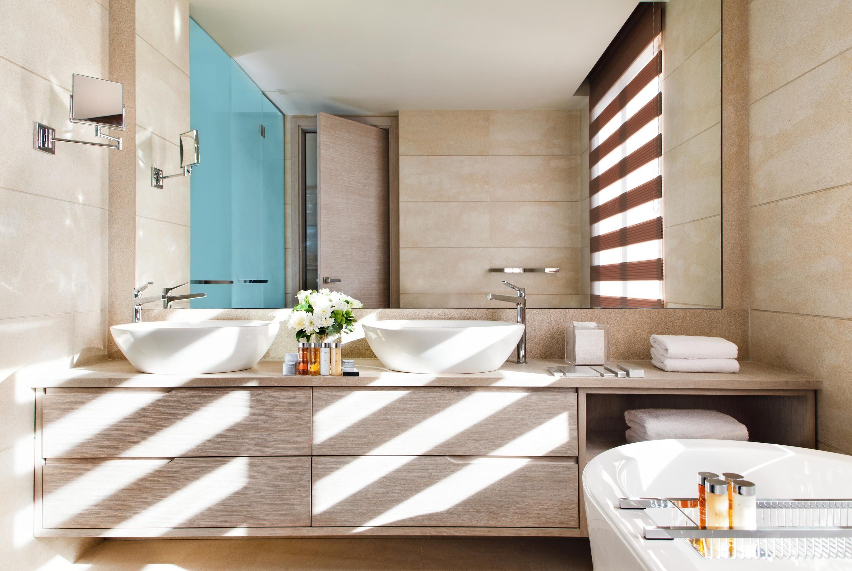 A modern bathroom with two sinks, a large mirror, and a bathtub.