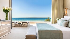 Un hotel moderno con una habitación amplia y ventana con vistas al mar, cama bien hecha, un pequeño rincón de descanso con una mesa y un florero.