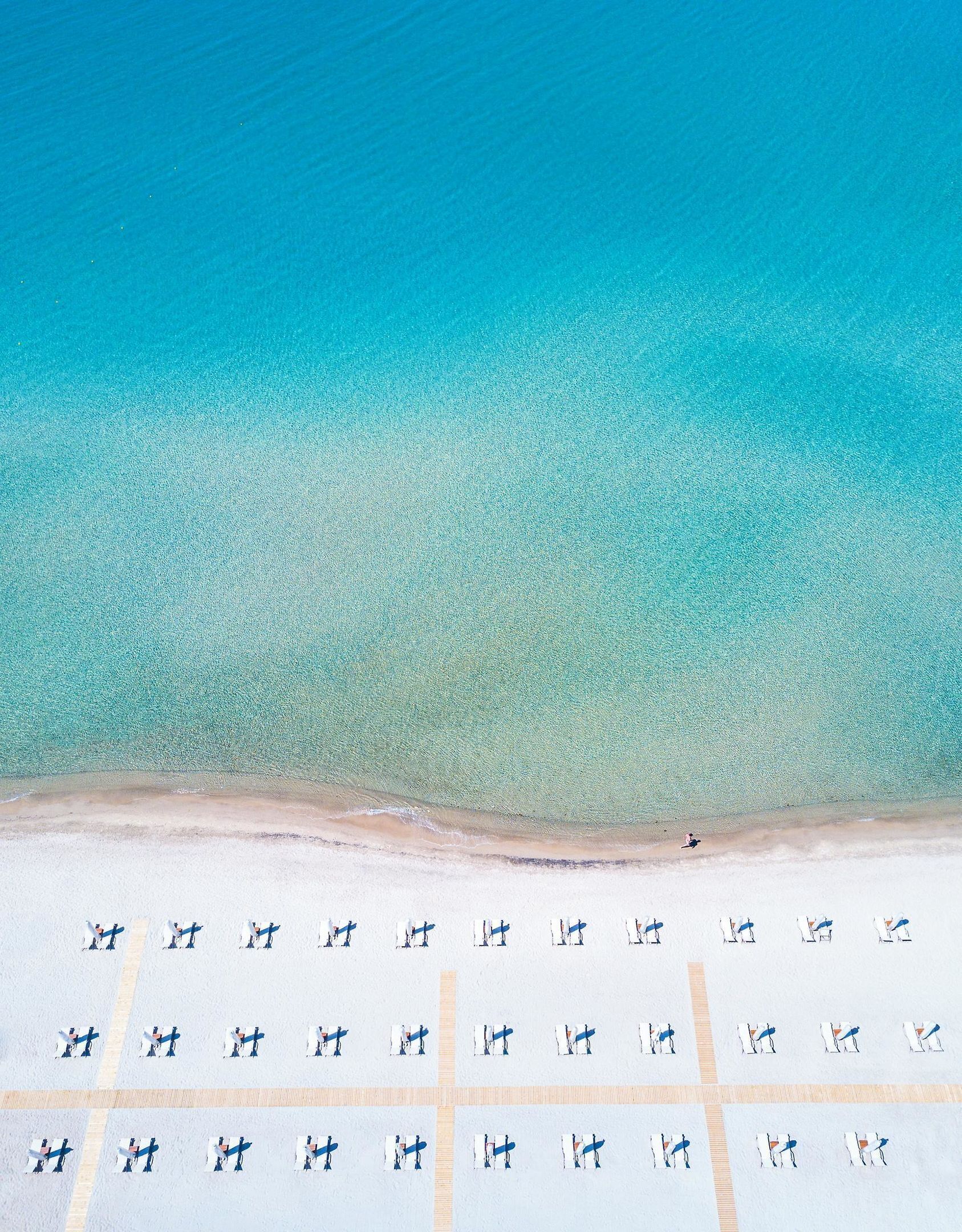Vista aérea de una playa con hileras de sillas y sombrillas.