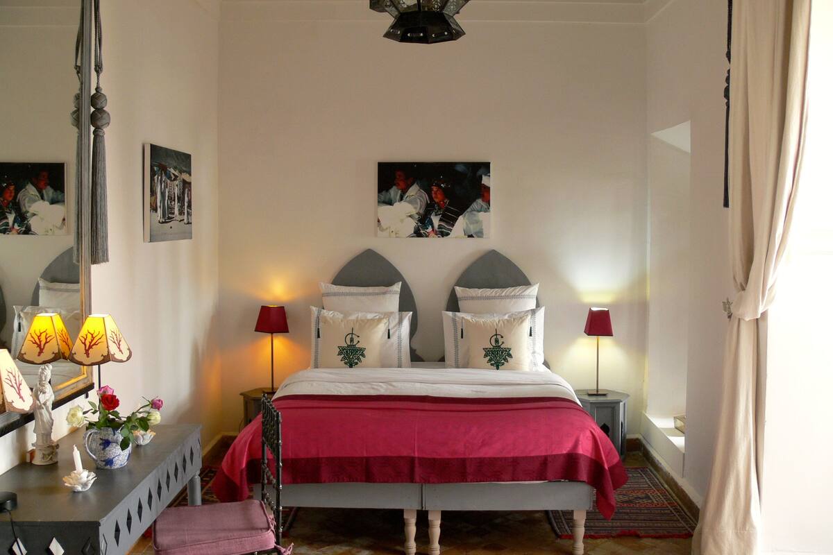 A bedroom with a bed, bedside lamps, a mirror, and artwork on the walls.