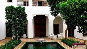 A courtyard with a pool, two white wicker chairs, a small table, and a large wooden door. - Riad El Mezouar (Marrakech)