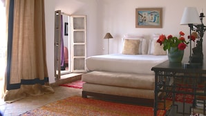 A bedroom with a bed, a nightstand, a lamp, a vase with flowers, and a painting on the wall. - Riad El Mezouar (Marrakech)