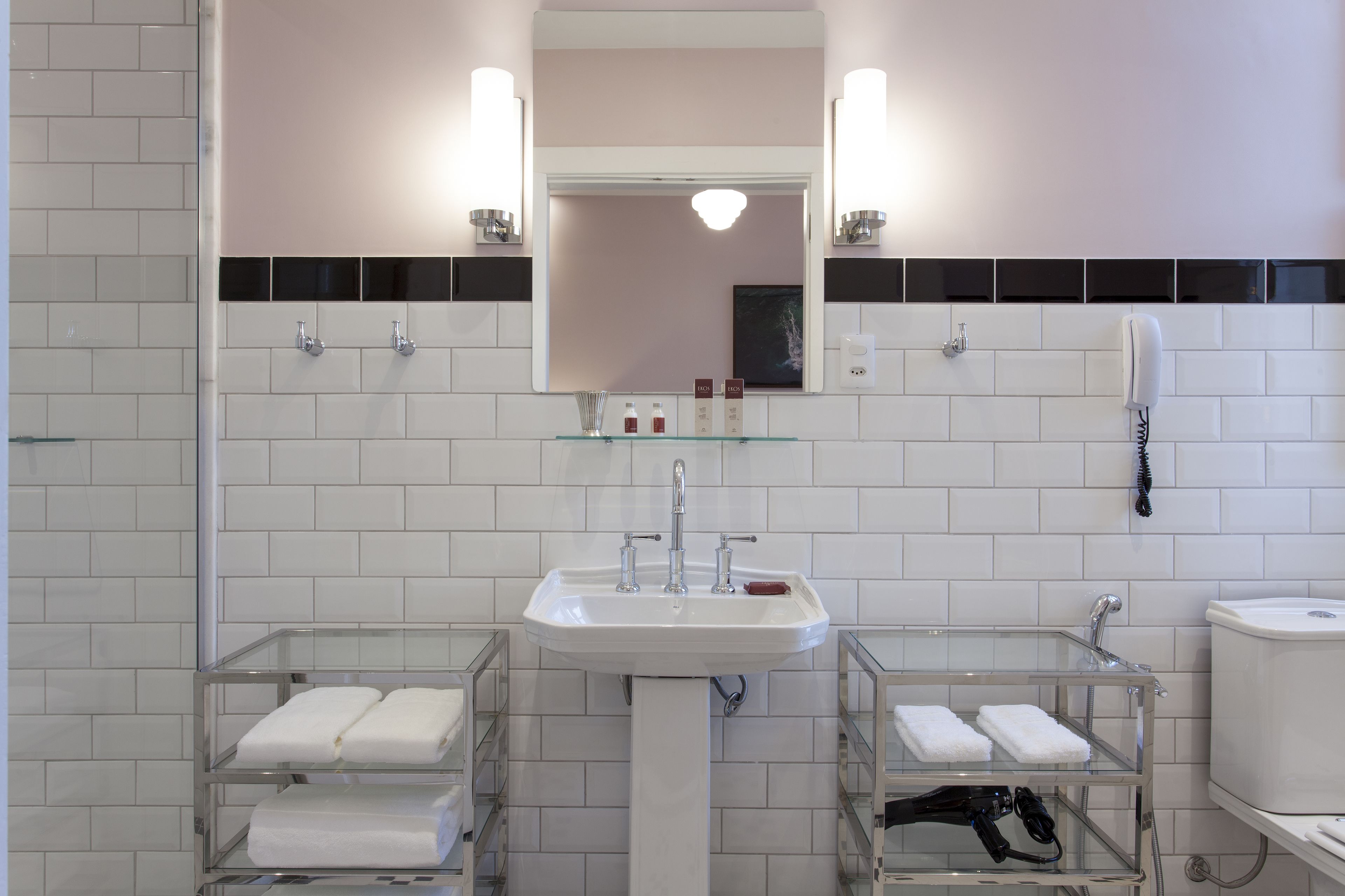 A bathroom with a white sink, two glass shelves with towels, a mirror, and a toilet.