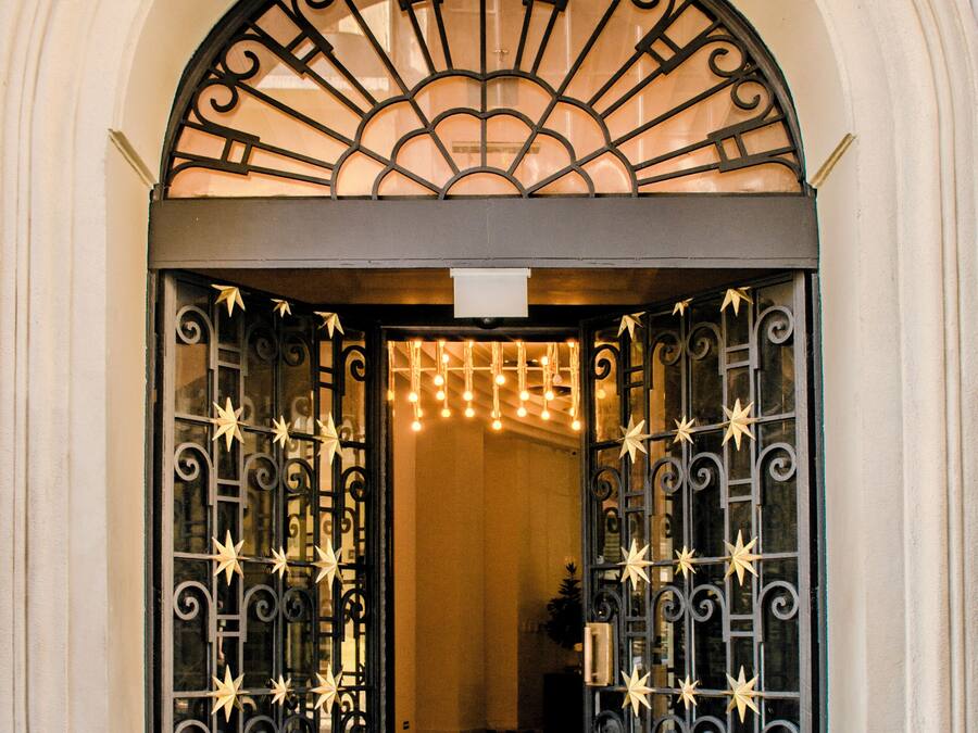 Una entrada imponente con una reja de hierro negro, suelo a cuadros y un arco blanco ornamentado.