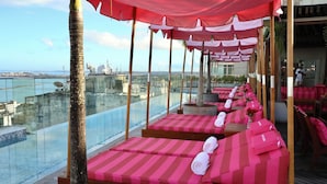 A rooftop lounge with striped red and pink cushions, a palm tree, and a view of the city skyline. - Fera Palace Hotel (Salvador)