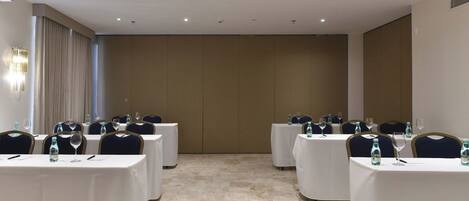 Un salón de conferencias con varias mesas, cada una dispuesta con sillas y botellas de agua.