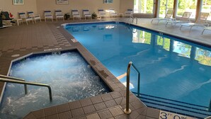 An indoor swimming pool with lounge chairs and a hot tub area.