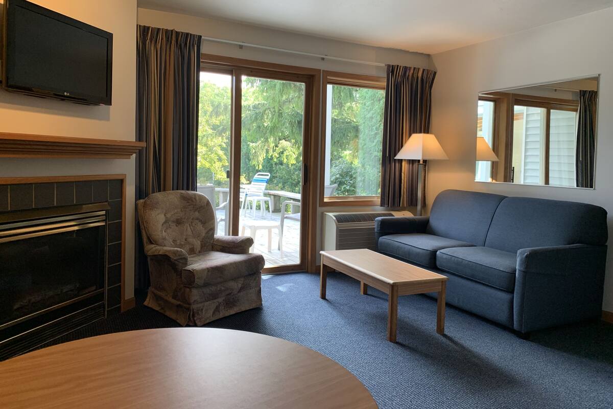 Ein Wohnzimmer mit Kamin, einer Couch, einem Sessel, einem Tisch und einem Fernseher.