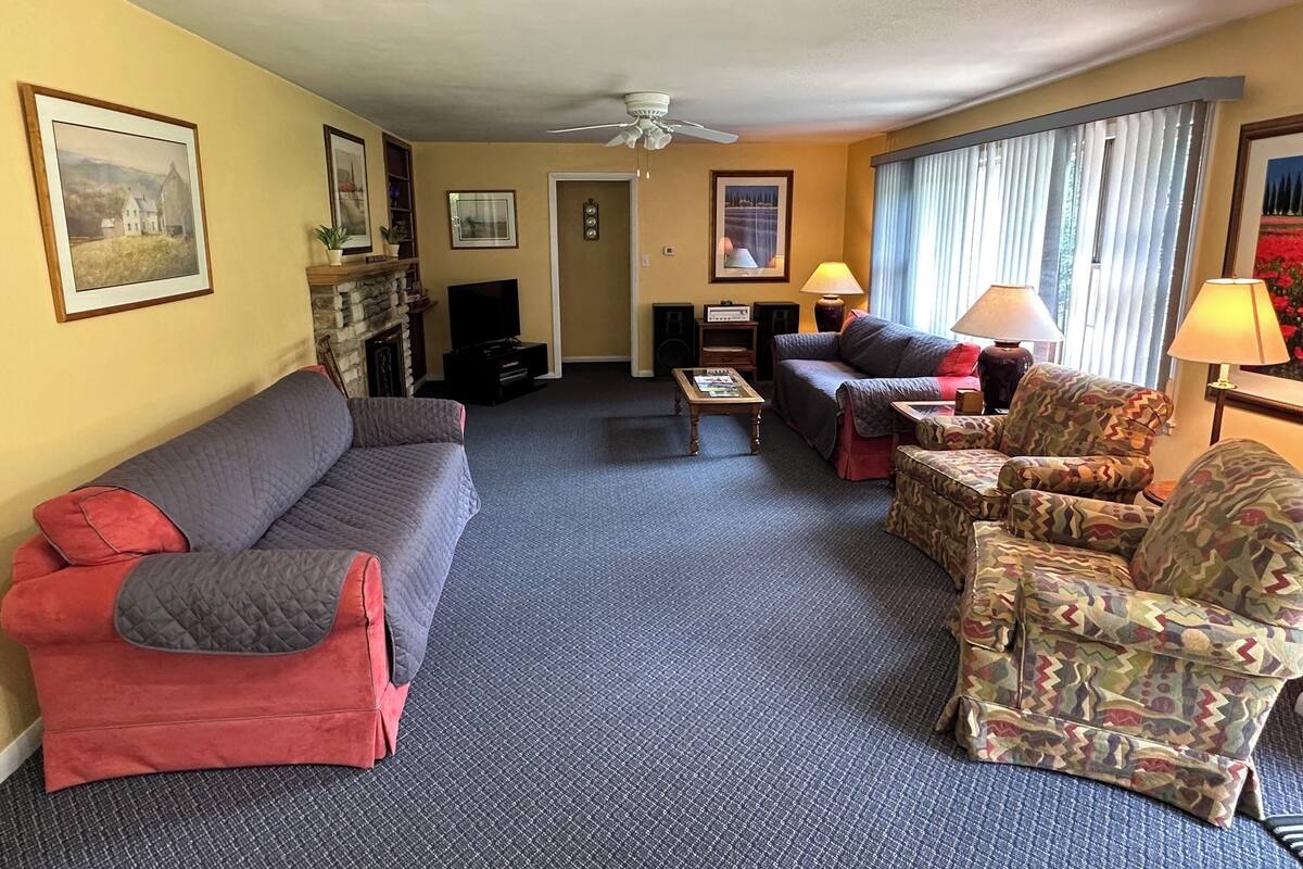 Ein Wohnzimmer mit einer Couch, Sesseln, einem Couchtisch, einem Fernseher und einem Kamin.