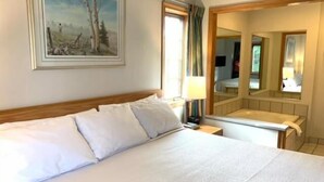A hotel room with a bed, a nightstand, a mirror, and a painting on the wall.