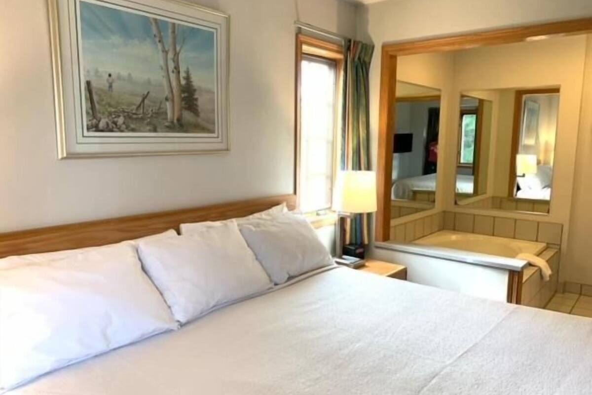 Ein Hotelzimmer mit Bett, Nachttisch, Spiegel und einem Gemälde an der Wand.