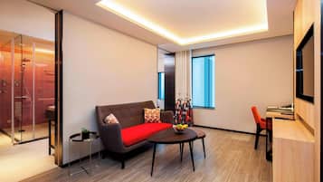 A modern hotel room with a sofa, a small table with fruit, a TV, and a desk.