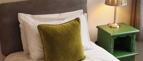 A bed with white bedding and a green pillow, a green bedside table with a lamp, and a grey headboard.