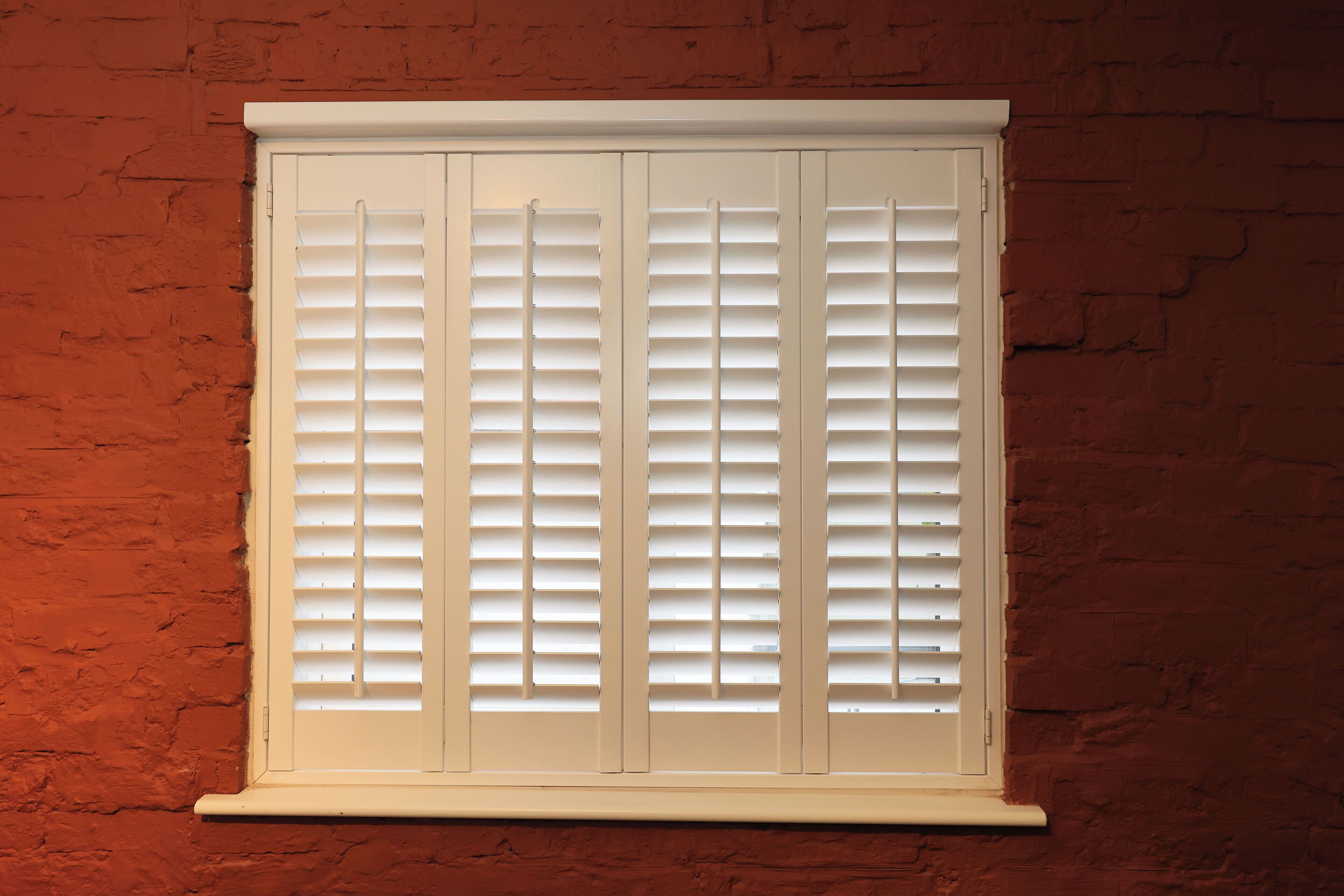 A window with white shutters against a brick wall.