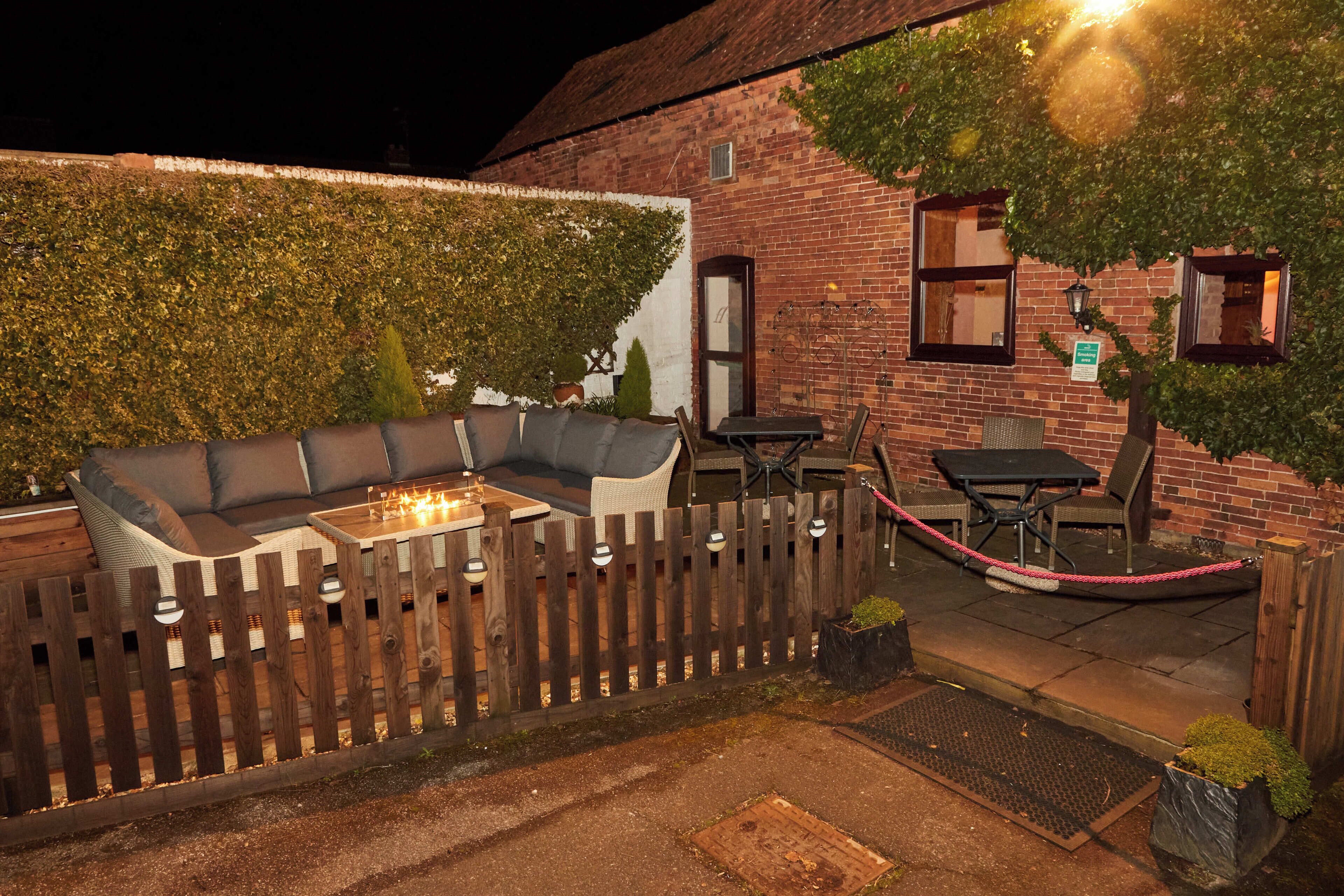 An outdoor seating area with a wooden fence, a brick building, and a table with chairs.