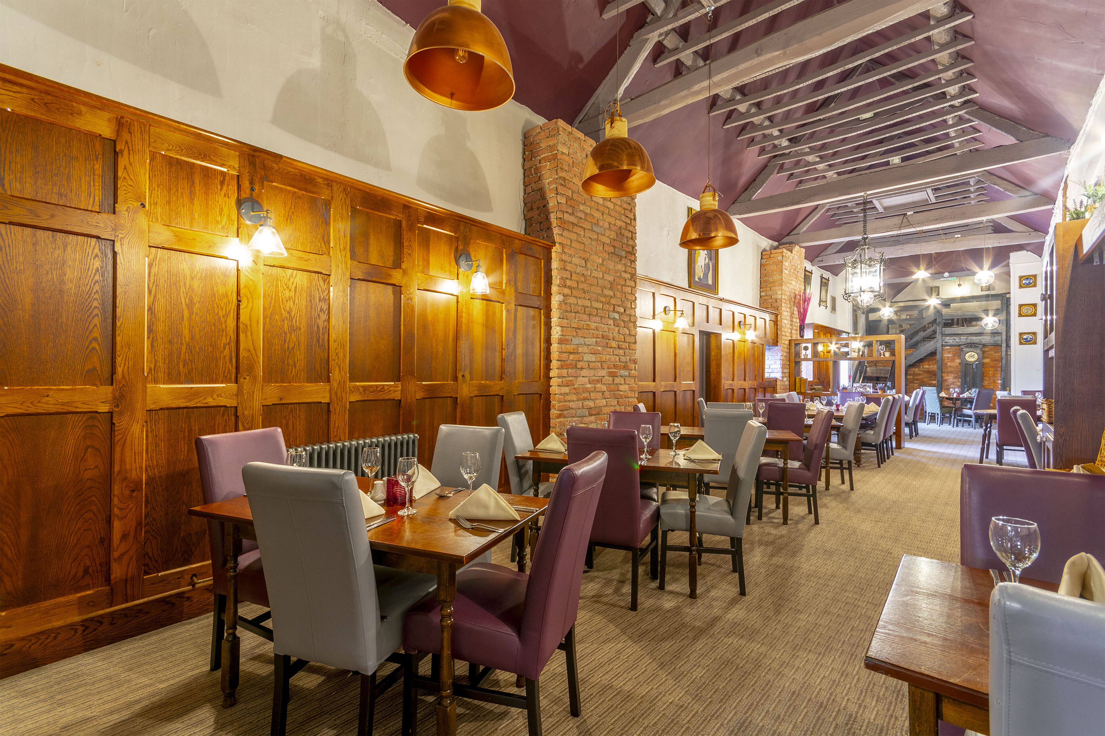 A restaurant with wooden paneling, brick walls, and pendant lighting. Tables are set with chairs and wine glasses.