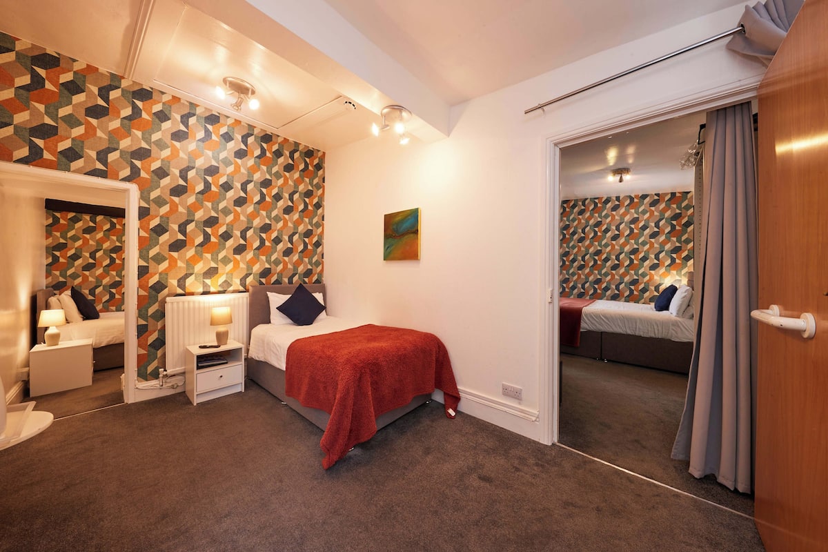 A bedroom with a bed, bedside tables, a mirror, and a door leading to another room.